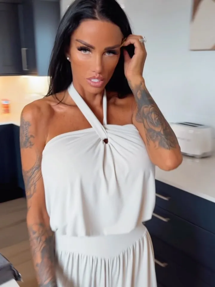 Katie Price in a white dress, her bright, uniform smile visible