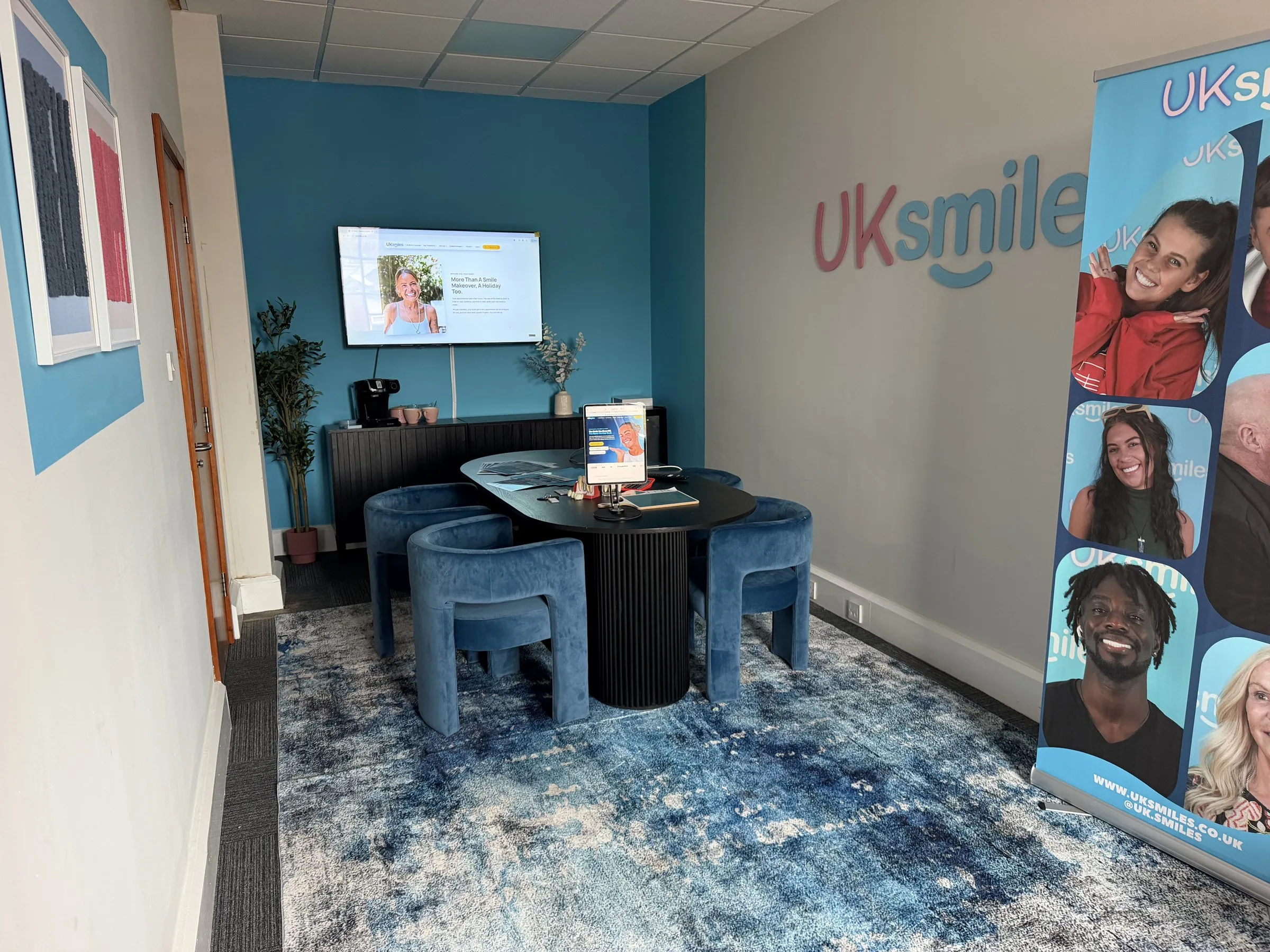 The UK Smiles consultation room in Leeds, with blue velvet chairs, an oval table and the UK Smiles logo on the wall