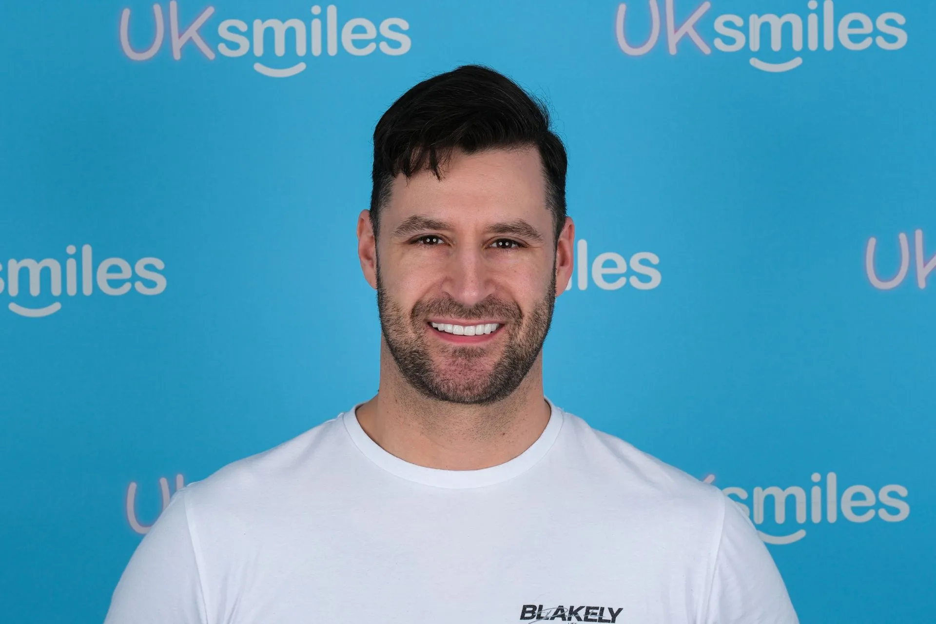 Smiling man in a white T-shirt in front of the UK Smiles backdrop