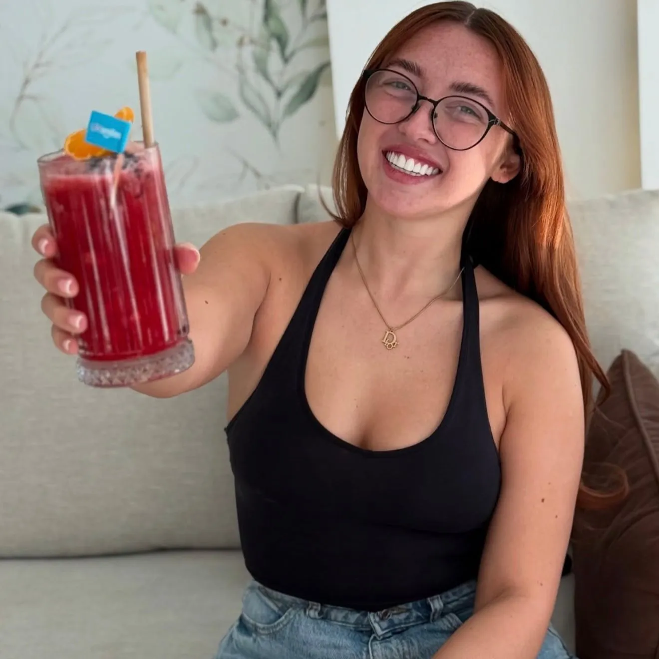 Red-haired woman with glasses raising a cocktail and smiling with her new teeth