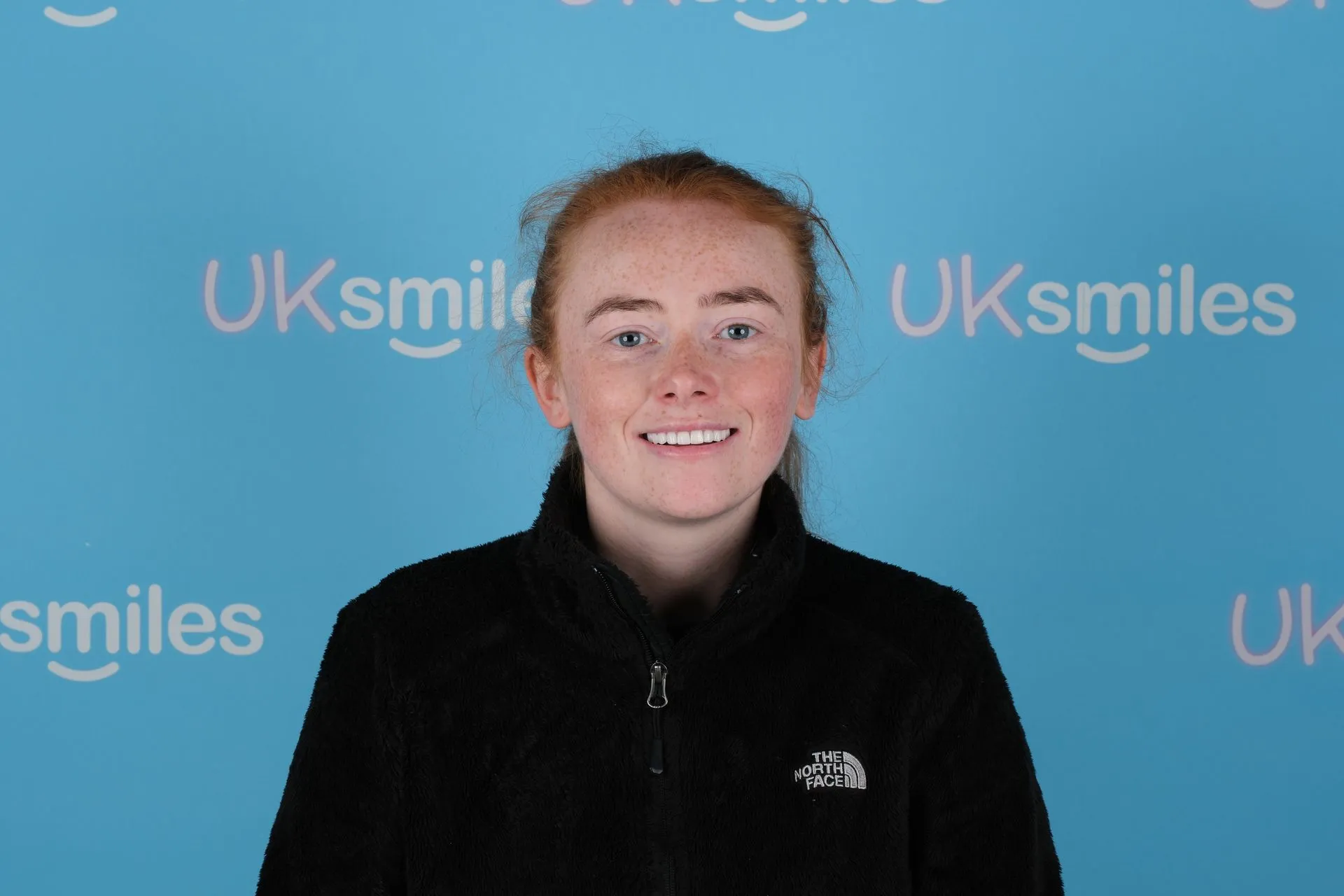 Red-haired woman smiling in front of the UK Smiles backdrop