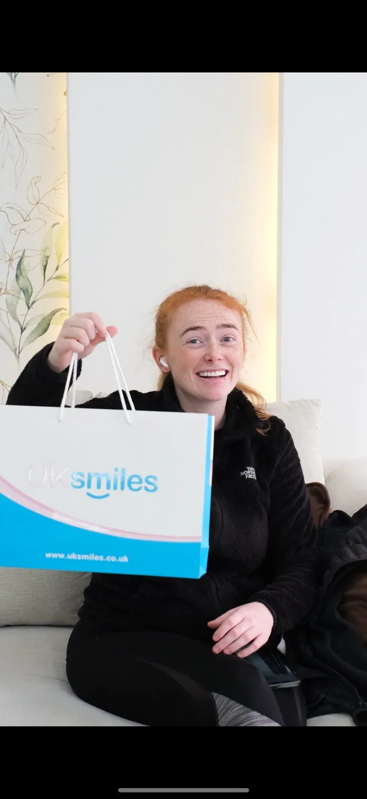 Red-haired woman holding a UK Smiles gift bag after her treatment