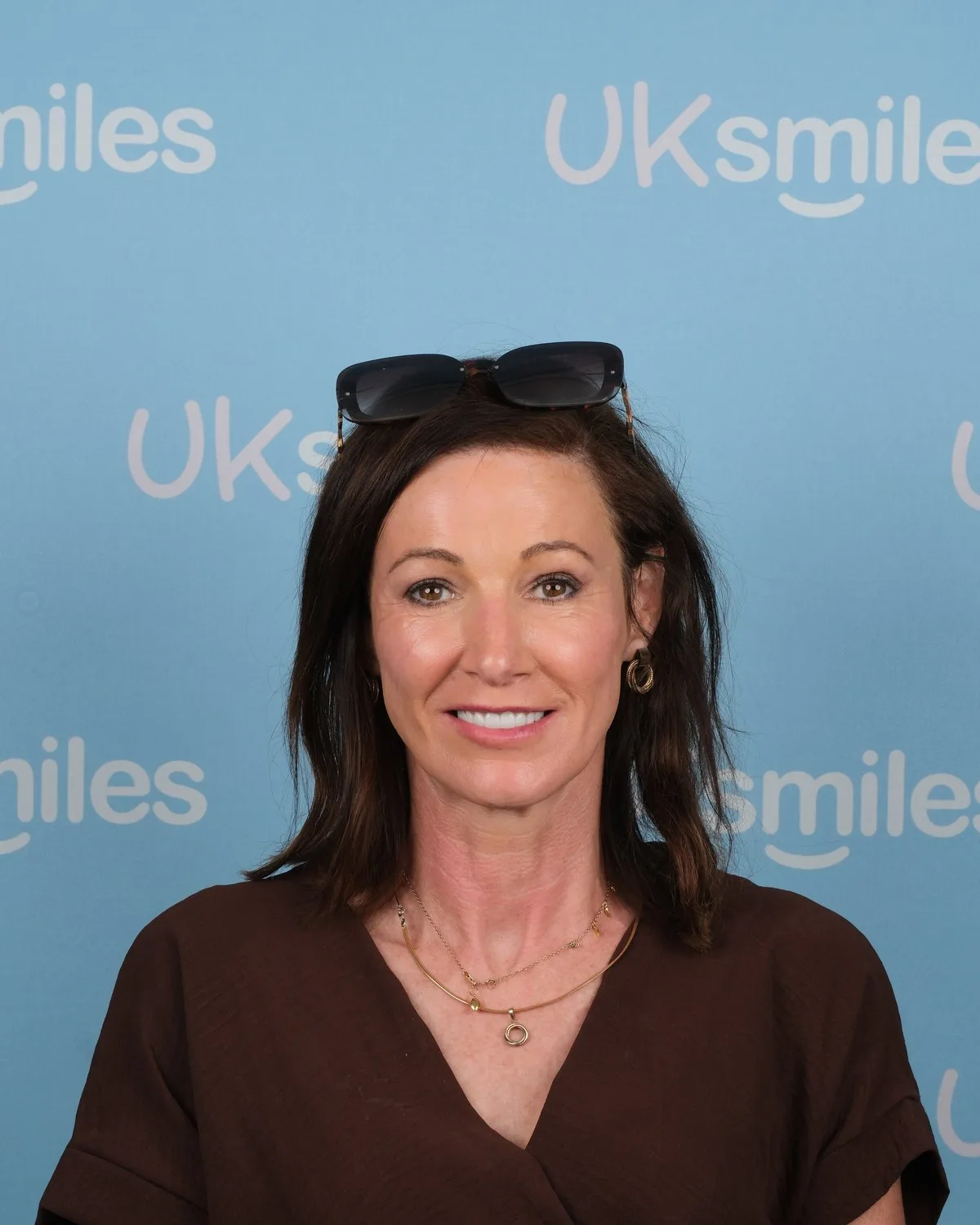 UK Smiles patient smiling after a full smile makeover, photographed in front of the cyan UK Smiles backdrop in Antalya.