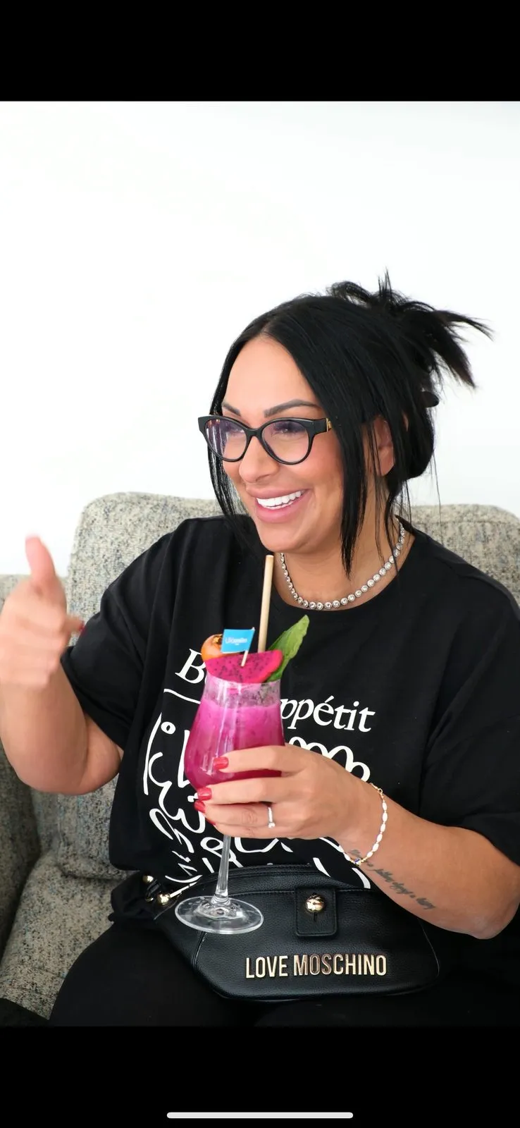 Woman with glasses holding a pink drink and showing her new smile